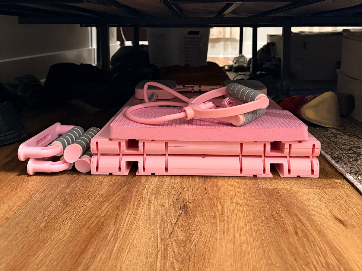 Folded pink Flo portable Pilates reformer under a sofa